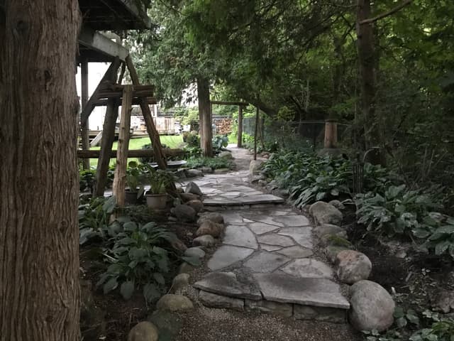 Flagstone path winding through the shade garden, edged with fieldstone boulders and a gravel margin. — Barrie, Ontario