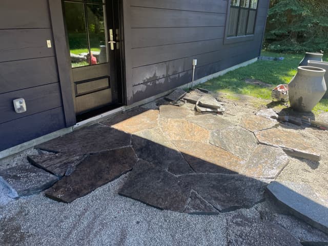 Granite flagstone going down over the compacted HPB base, with offcuts stacked to one side for the next run. — Collingwood, Ontario