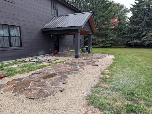 Granite flagstone laid out from the entry, with the next run of stone stacked ready on the grass. — Collingwood, Ontario