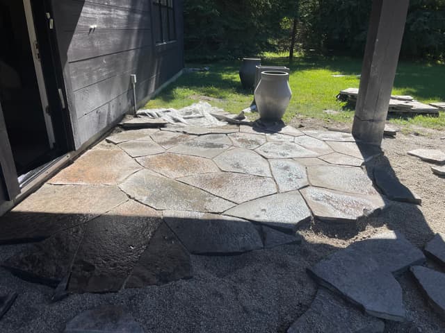 Granite flagstone laid up to the wall of the house, the field fitted tight and bedding gravel still open along the edges. — Collingwood, Ontario