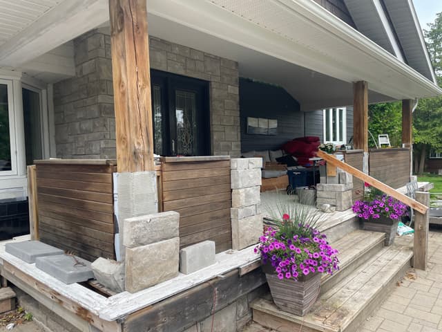 Cut stone facing built up around the porch piers, with rough timber posts and horizontal wood slat privacy panels. — Georgian Bay, Ontario