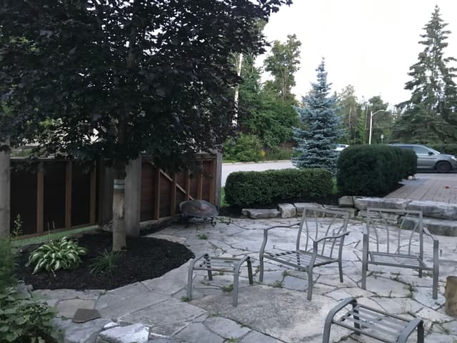 Irregular flagstone patio with tight-fitted joints, edged in armour stone alongside a wood board fence. — Barrie, Ontario