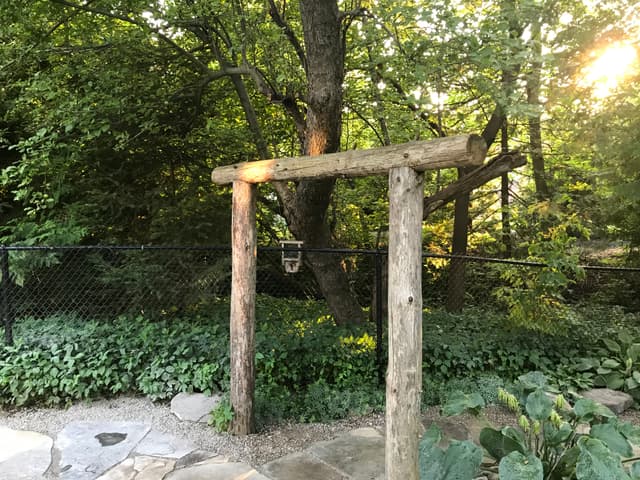 Peeled log arbour at the garden entry, two round posts carrying a heavy log header over the flagstone. — Barrie, Ontario
